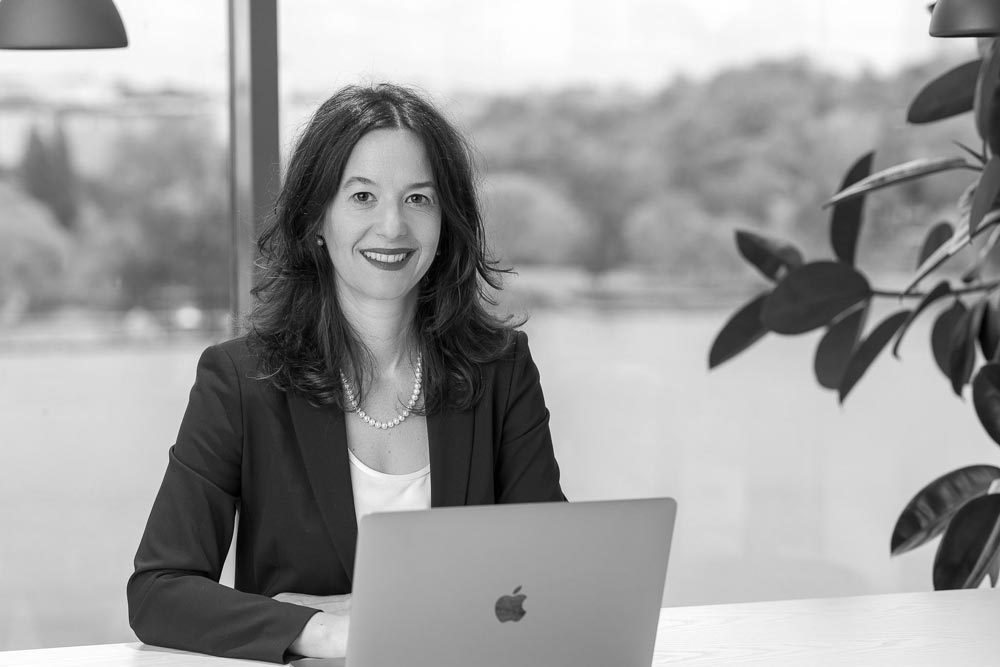 Gordana sitter vid en dator och ler mot kameran