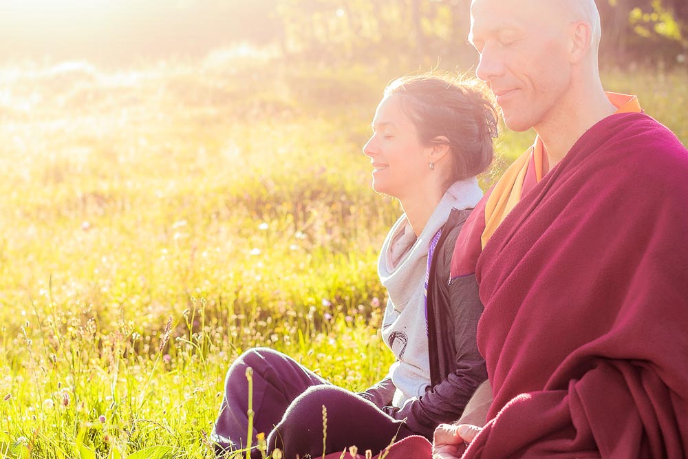 Gordana och en man sitter på en äng i solen och mediterar